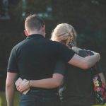 A couple with backs facing the camera, standing close with arms around each other, in a park.