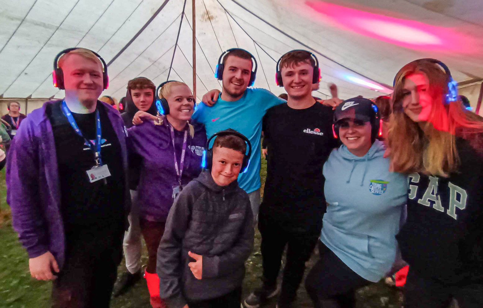 Group of young carers and leaders wearing headphones at a silent disco in a large tent.