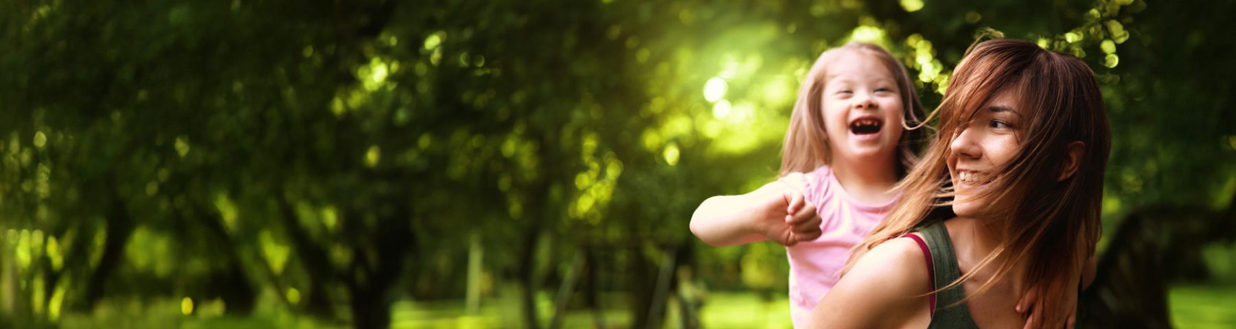 Woman giving a piggyback ride to a laughing child in a sunny, green park.