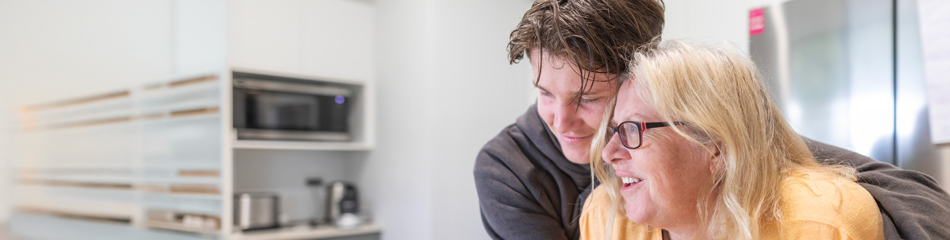 Man and woman smiling and embracing in a kitchen setting.