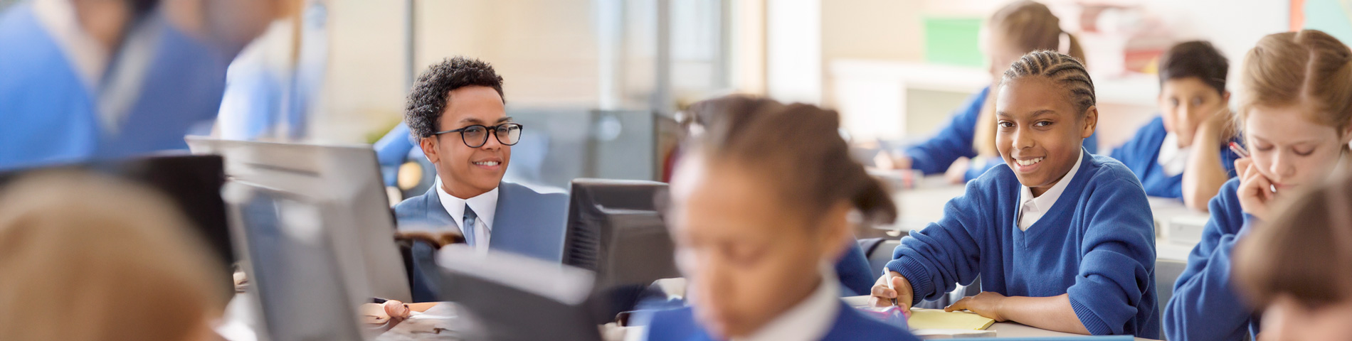 Students in blue uniforms are working in a classroom with laptops and notebooks.